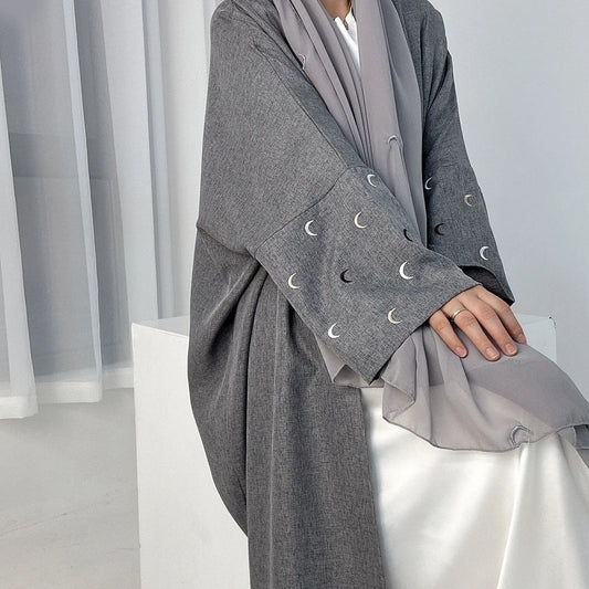 Person wearing a gray outfit with moon emblem details against a white curtain background