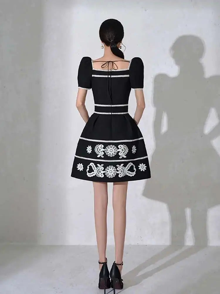 Black dress with white embroidery on a plain background