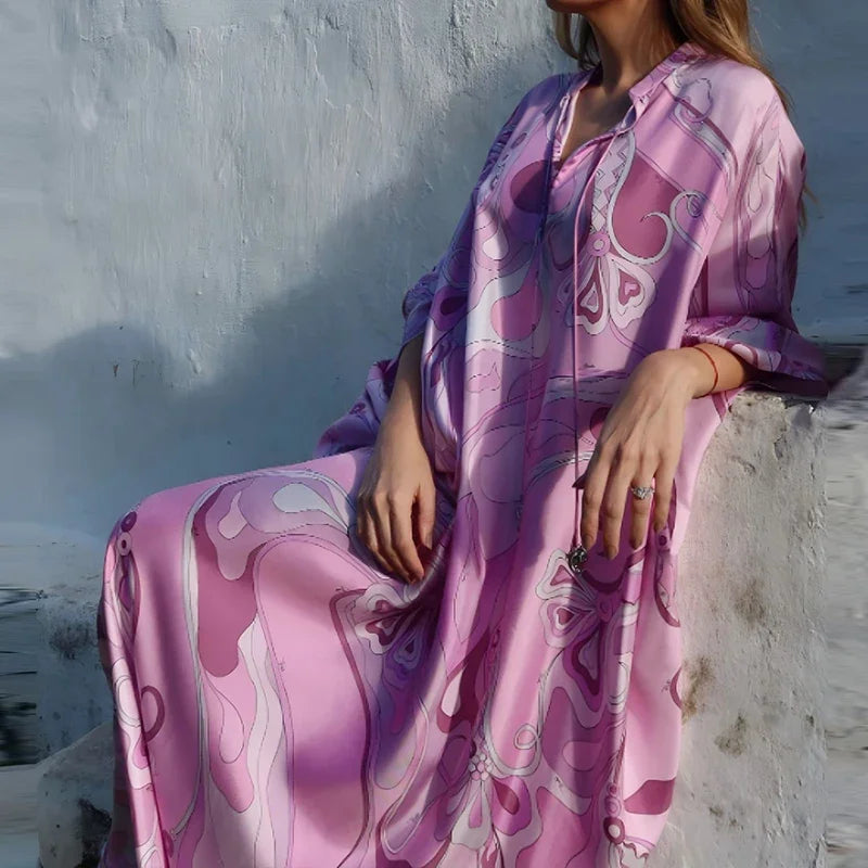 Person wearing a pink and purple patterned dress sitting against a light-colored wall.