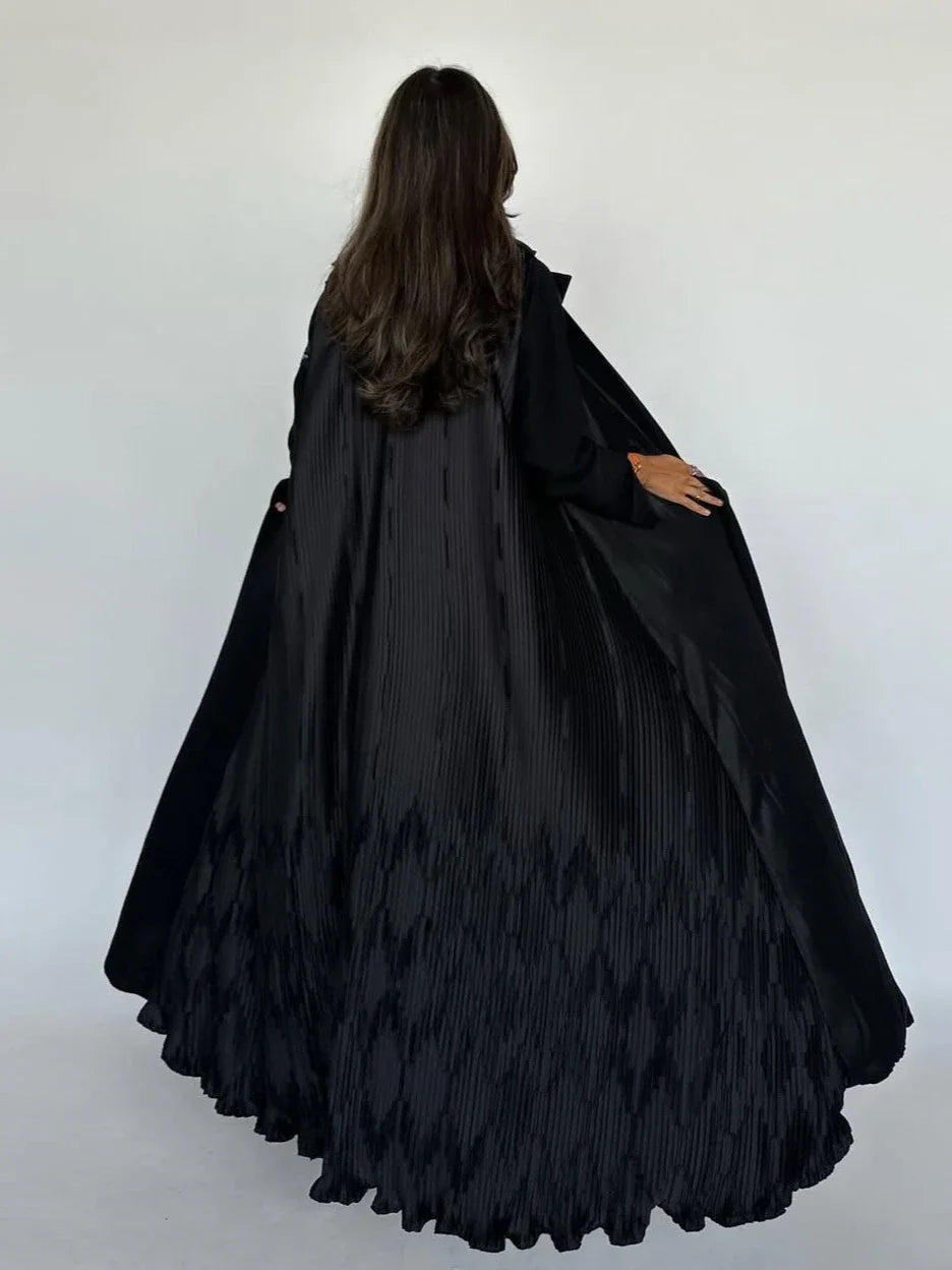 Person wearing a long black dress with feather details against a white background