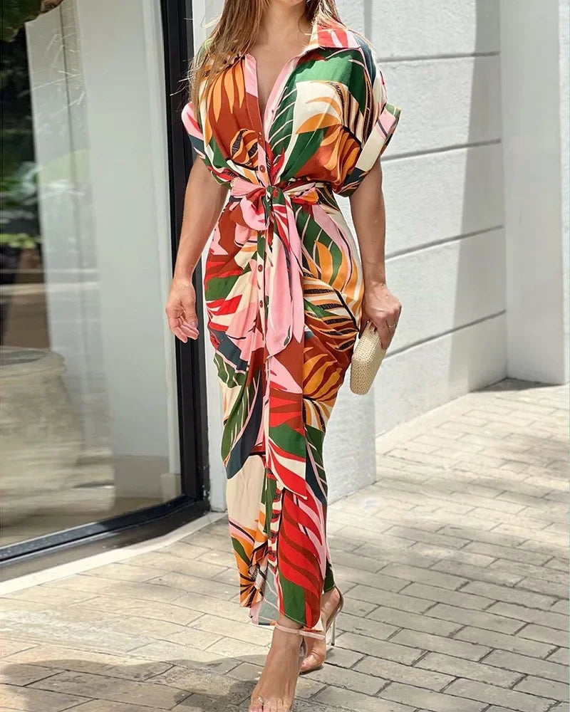 Woman wearing a colorful floral dress standing on a sidewalk.