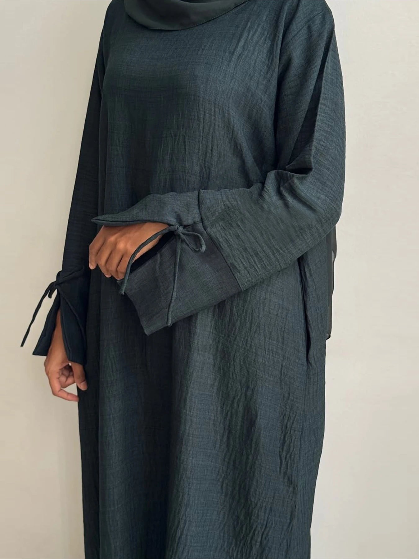 Person wearing a dark green abaya against a plain background