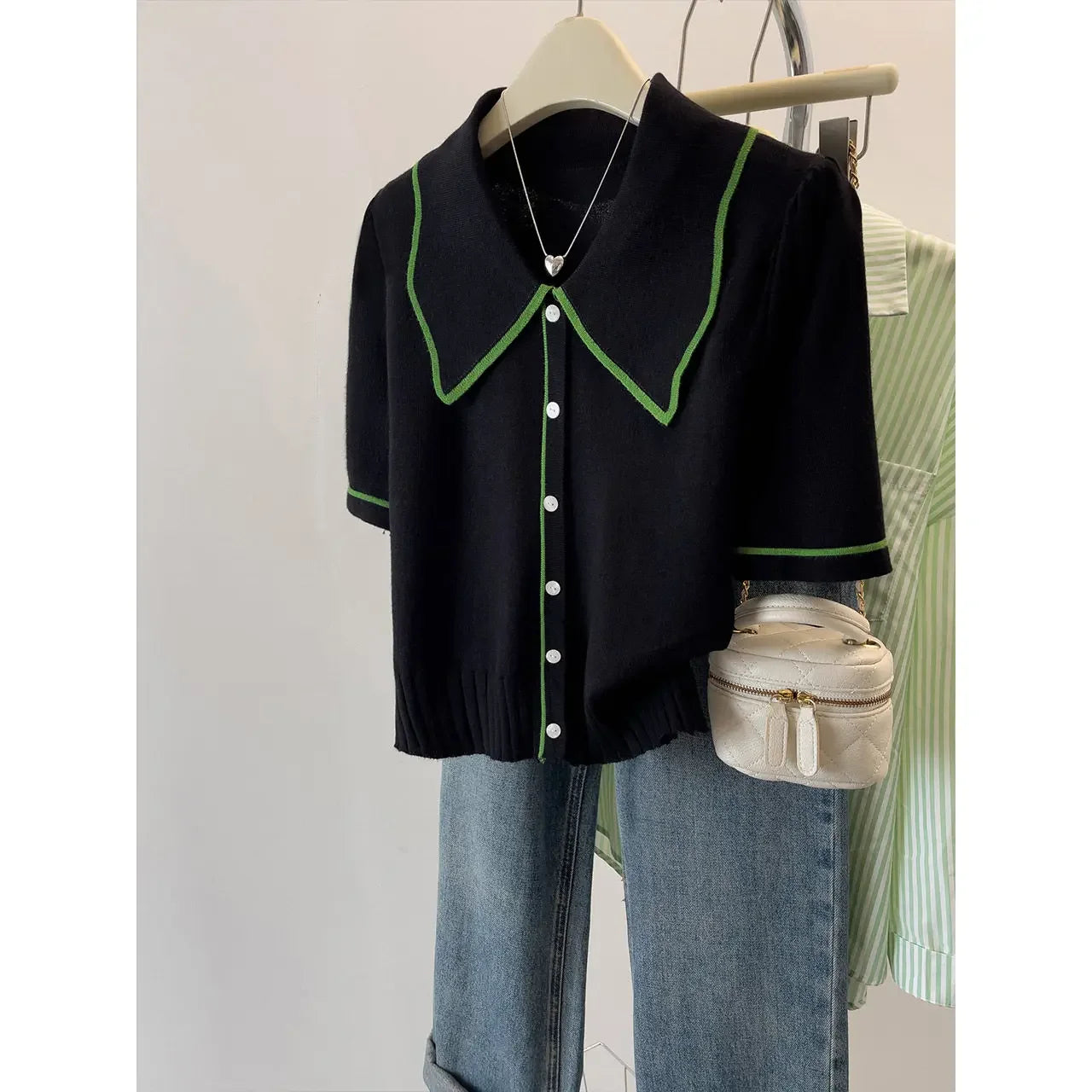 Black blouse with green accents on a hanger, paired with jeans and a small bag.