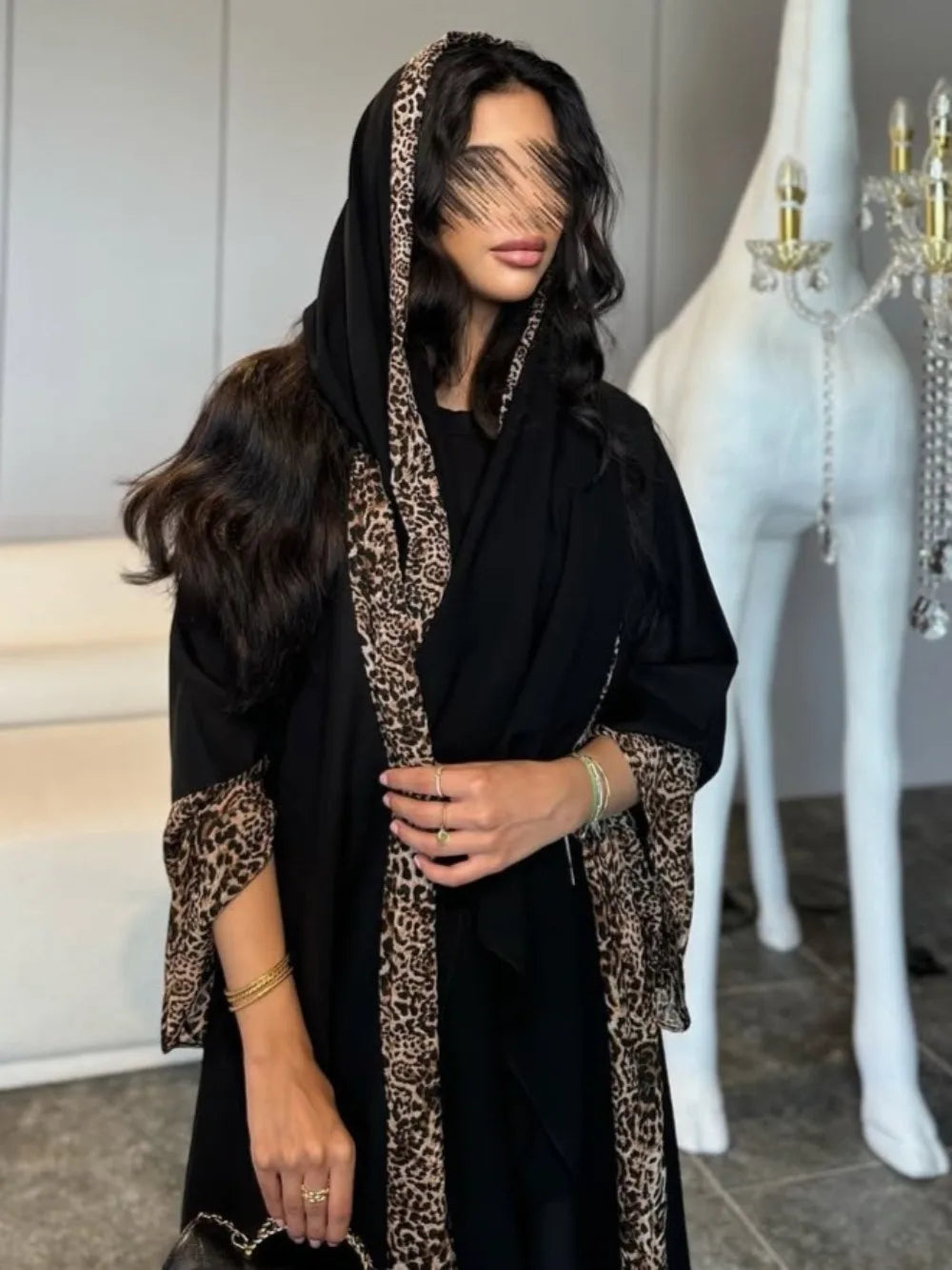 Woman wearing a black abaya with leopard print details in an indoor setting.