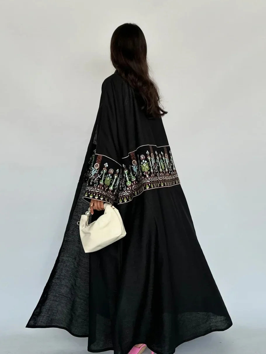 Person wearing a black embroidered dress holding a white clutch against a white background