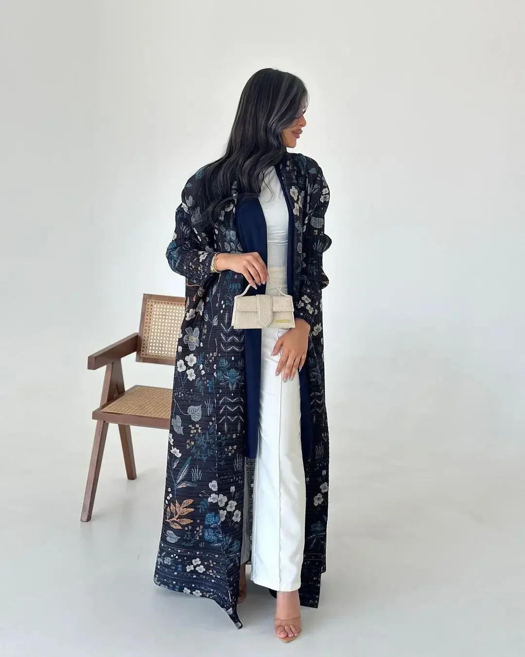 Woman wearing a long floral-patterned coat over a white dress, standing against a plain background.