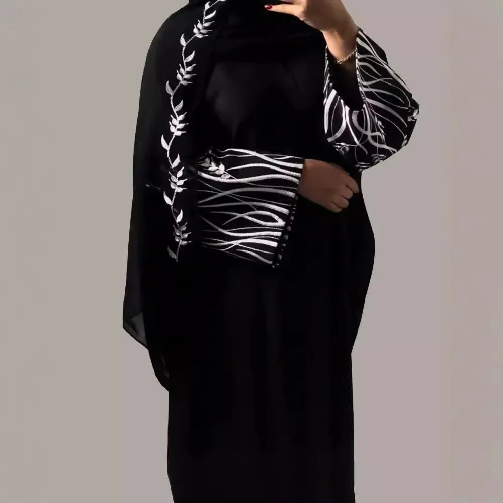 Person wearing a black outfit with white patterned sleeves against a plain background