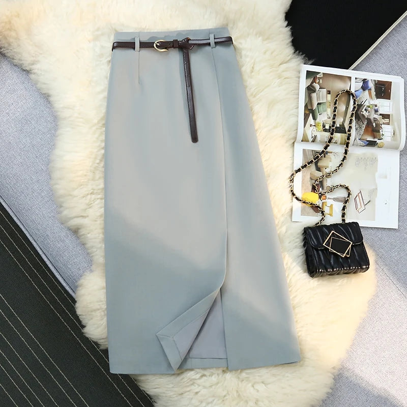 Light gray pants with a belt on a textured surface next to a magazine and handbag.