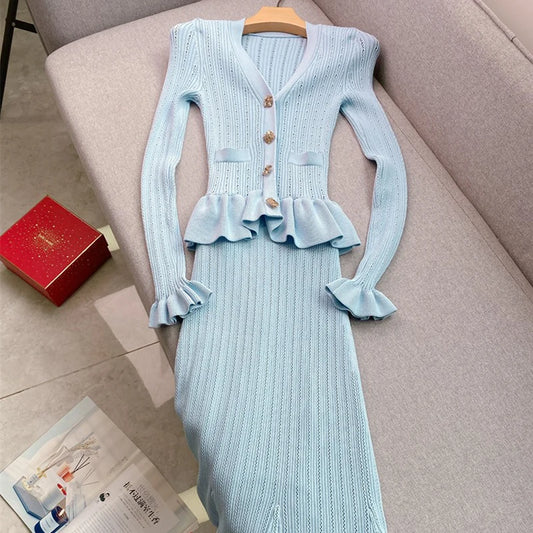 Light blue knitted dress with ruffled details on a hanger against a beige sofa.