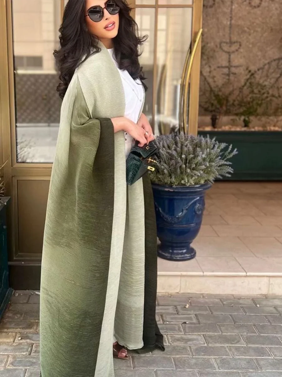 Woman in a long green coat holding a plant, standing in front of a building entrance.