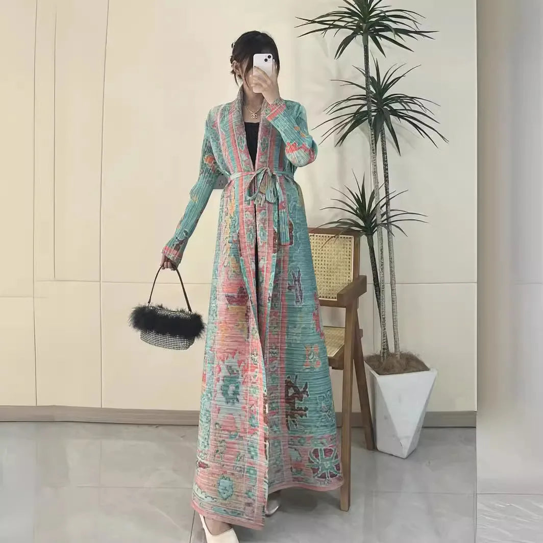 Person wearing a long, patterned coat in an indoor setting with plants and a chair.