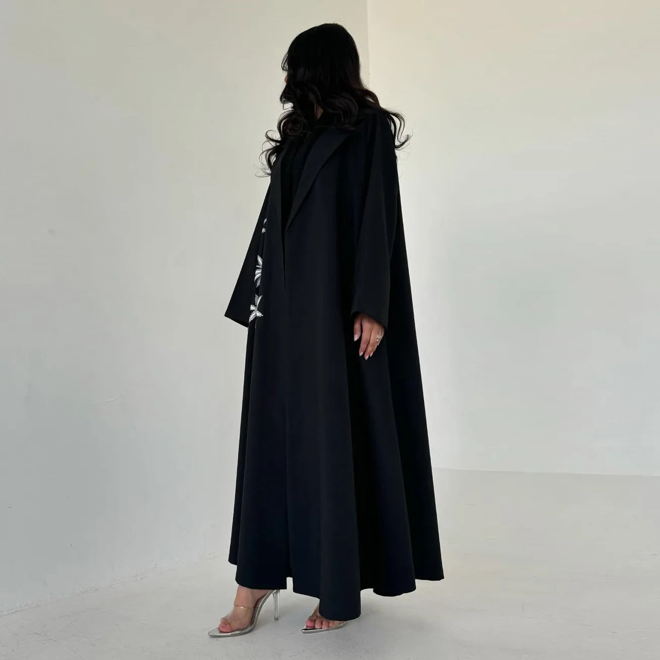 Person wearing a long black coat against a white background