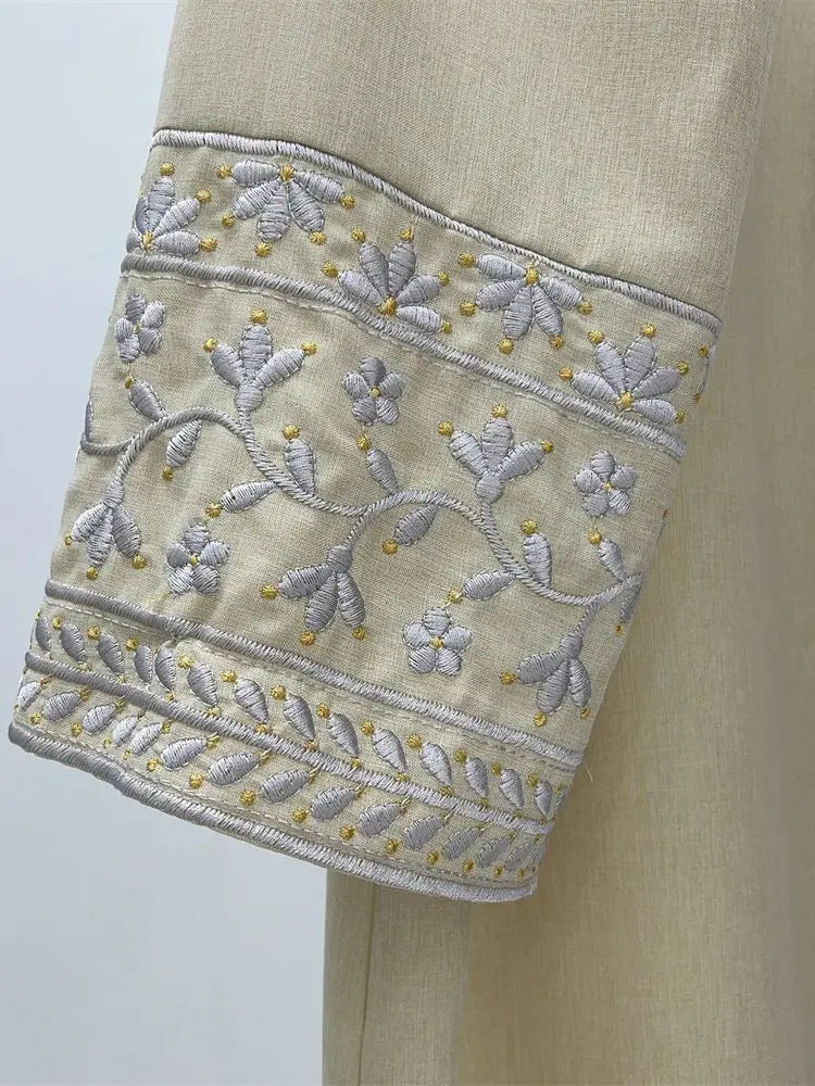 Close-up of beige fabric with intricate white floral embroidery on a light gray background
