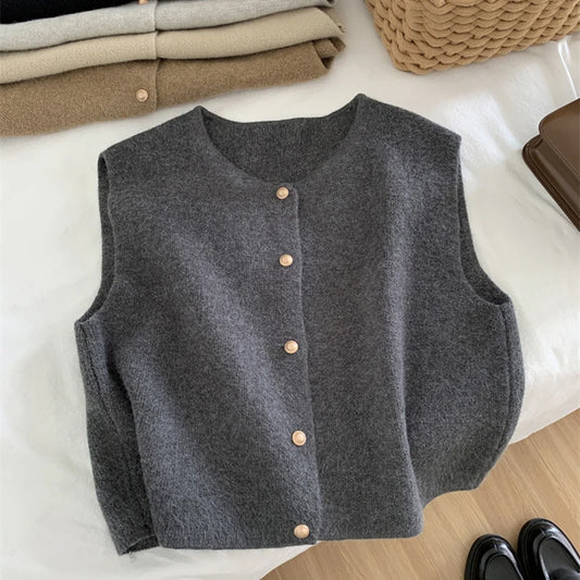 Gray button-up vest on a white surface with folded clothes and a woven basket in the background.