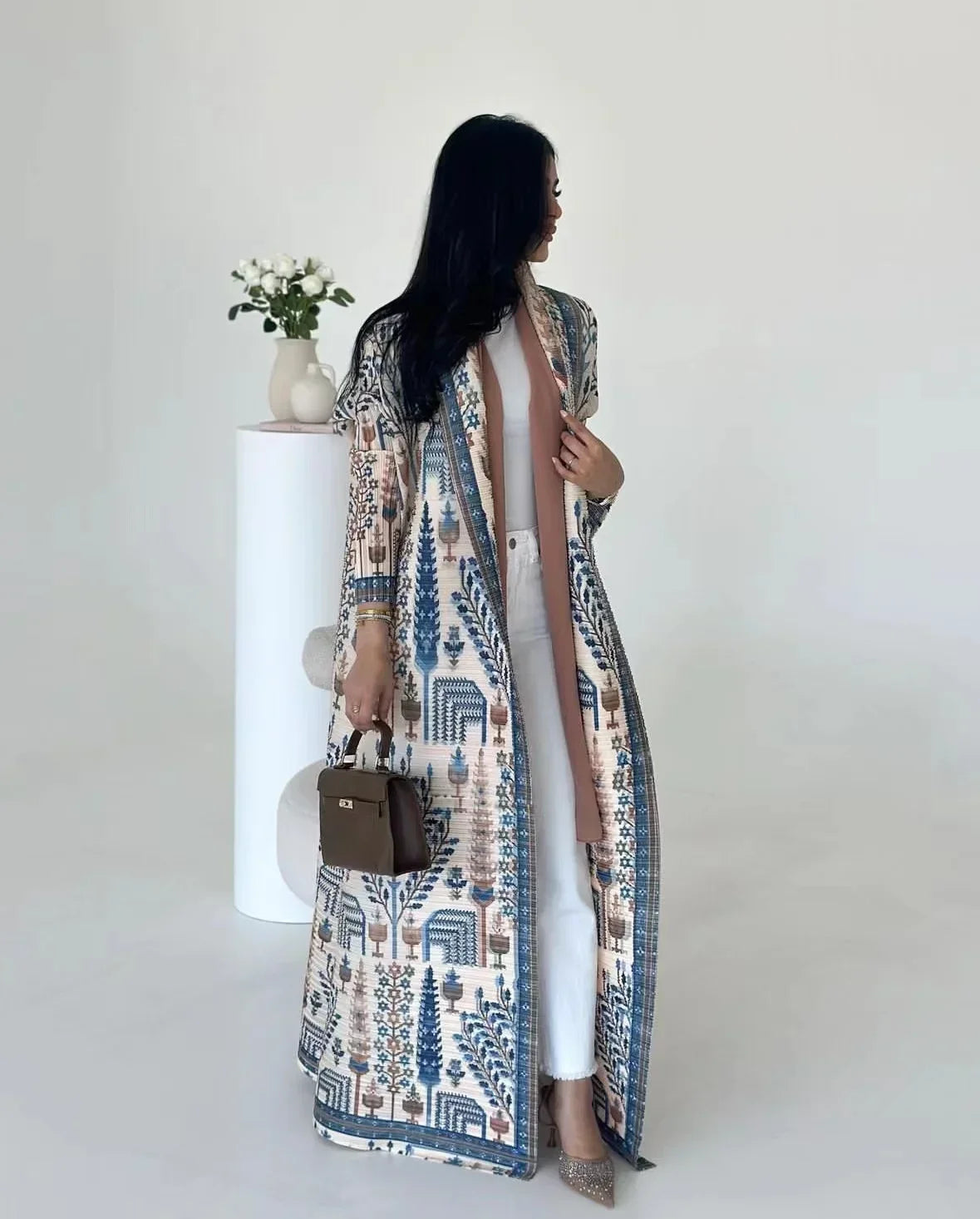 Woman wearing a long, patterned coat over a white dress on a plain background