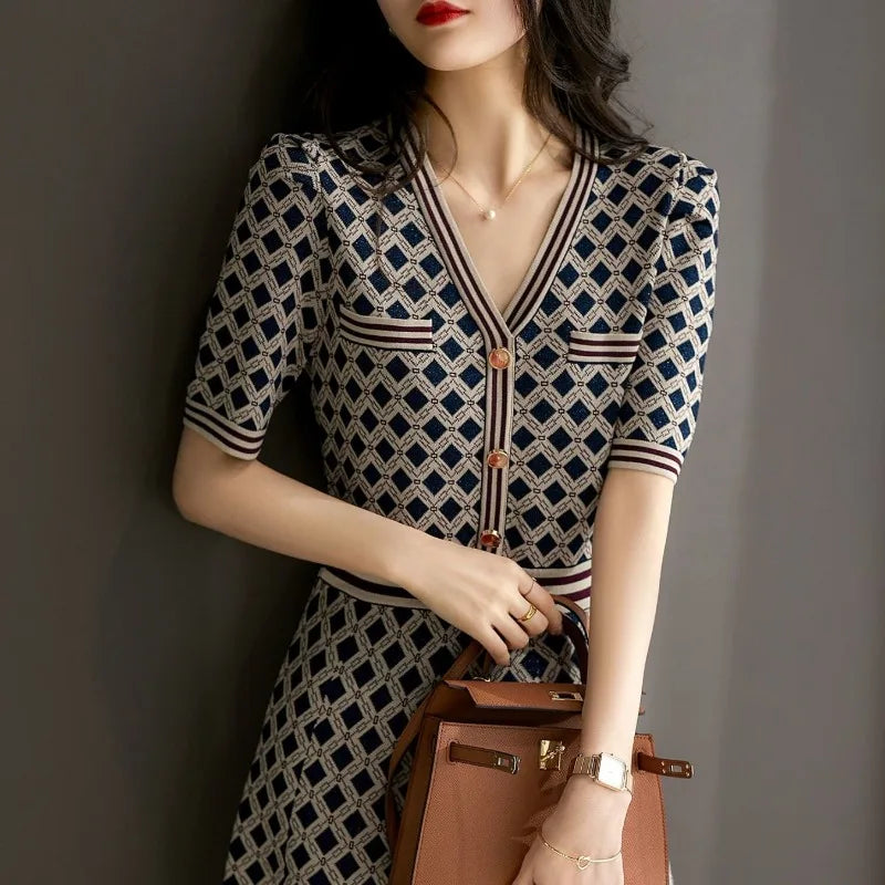 Woman wearing a patterned dress holding a brown handbag against a gray background