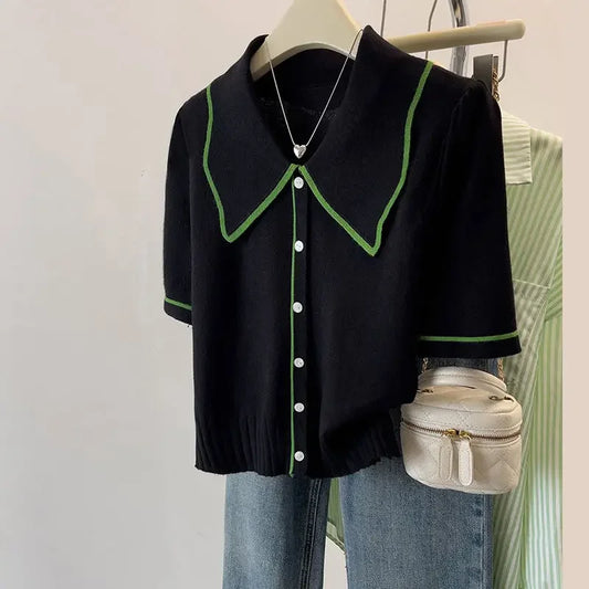 Black short-sleeve shirt with green trim on a hanger against a neutral background