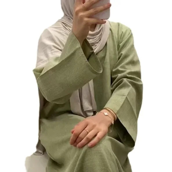 Person wearing a green outfit with a beige hijab on a white background