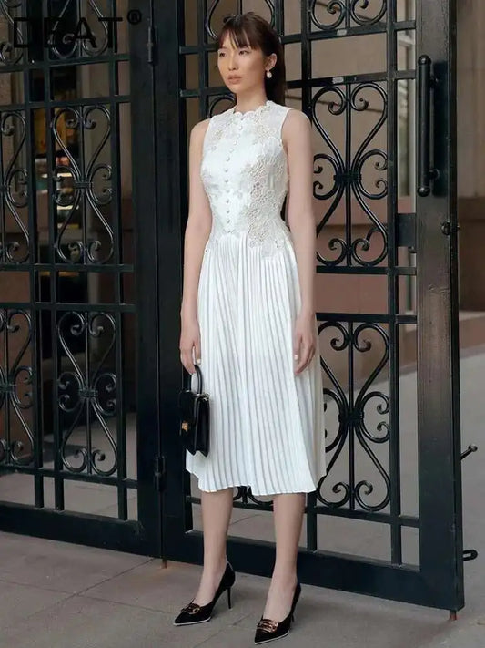 Woman in a white dress standing in front of an ornate black metal gate.