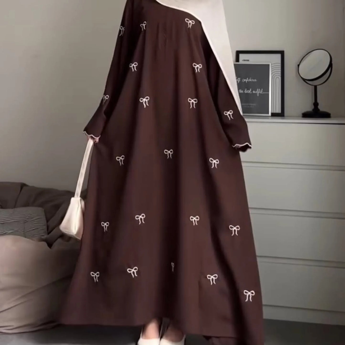 Brown dress with white bow patterns worn by a person, sitting on a bed in a room.