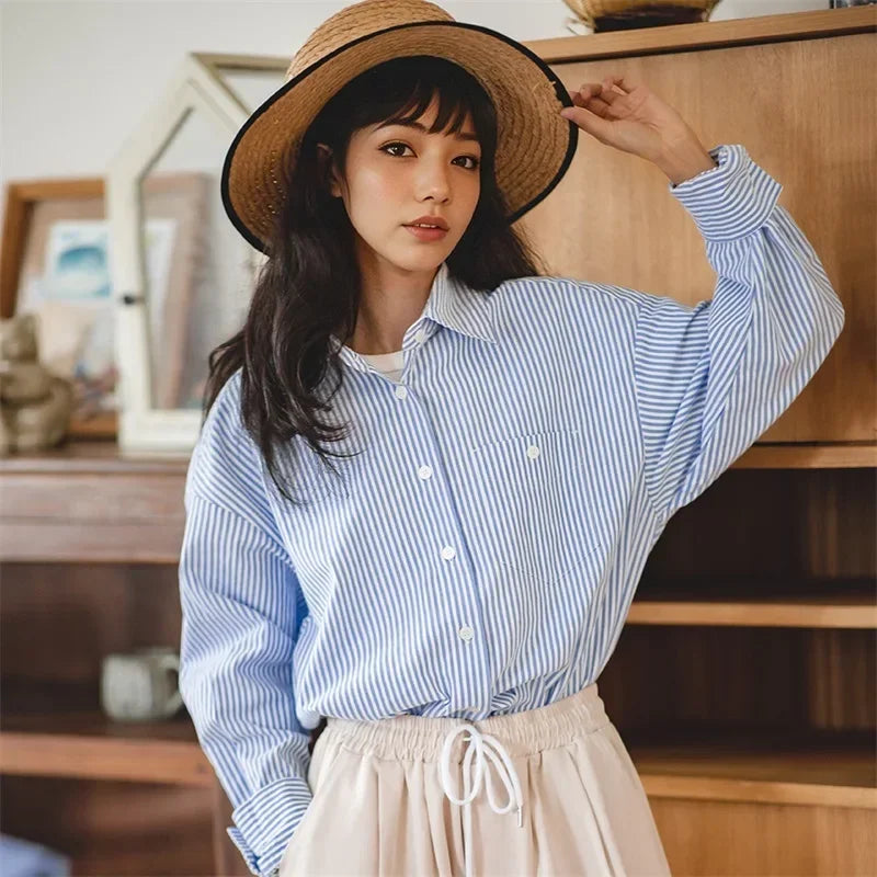 Woman wearing a straw hat and blue striped shirt in a room with wooden furniture.
