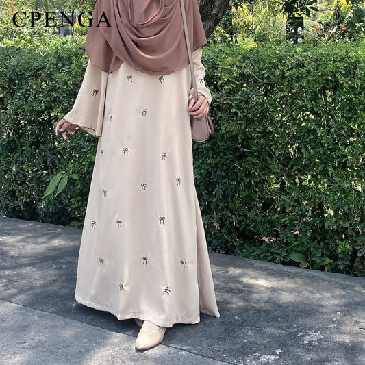 Woman wearing a beige dress with small patterns and a matching headscarf, standing outdoors.